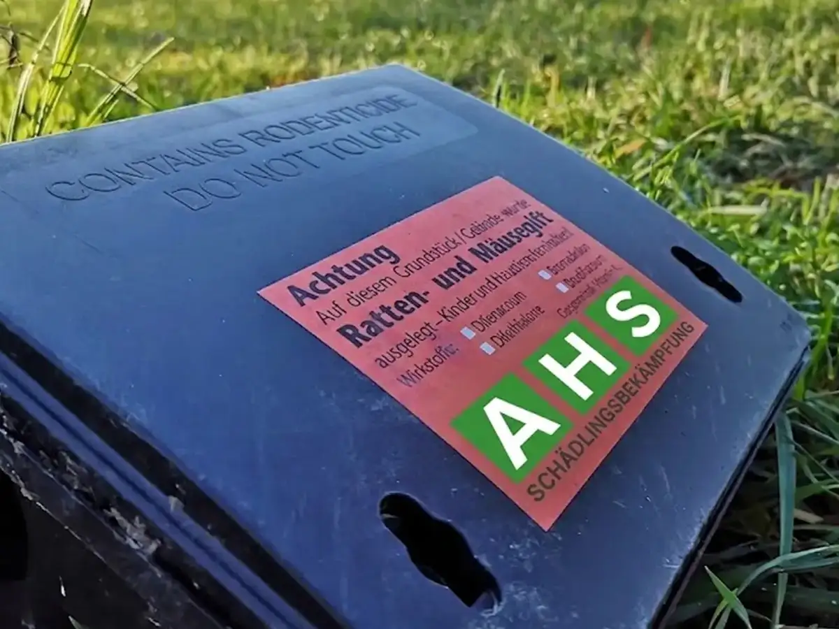 Manipulationssichere Köderstation der AHS Schädlingsbekämpfung auf einem Rasen, mit Warnaufkleber zu ausgelegtem Ratten- und Mäusegift und deklarierten Wirkstoffen